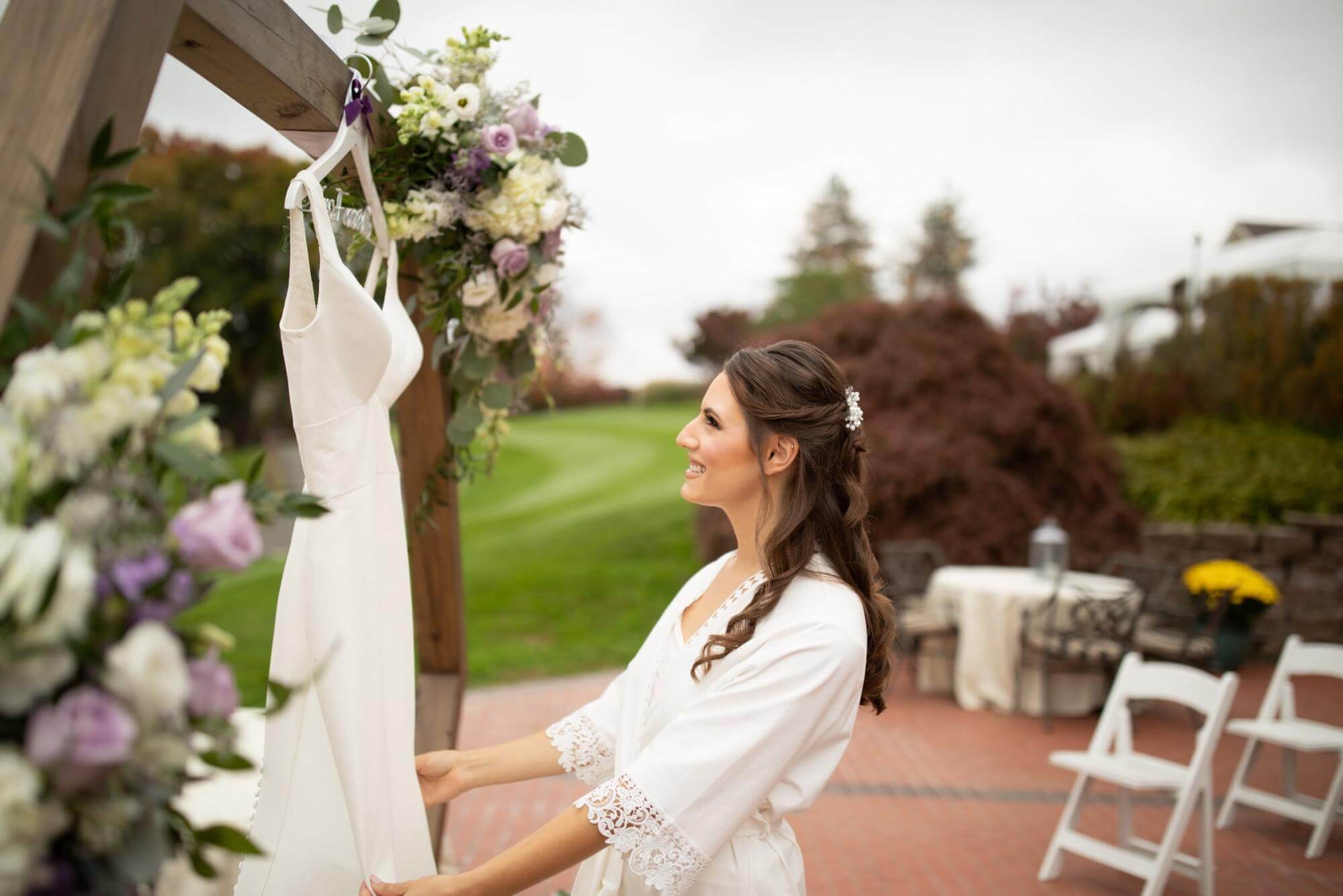 Beautiful bride standing outside at the wedding venue looking at her dress hanging up before her and preparing for the day's ceremony
