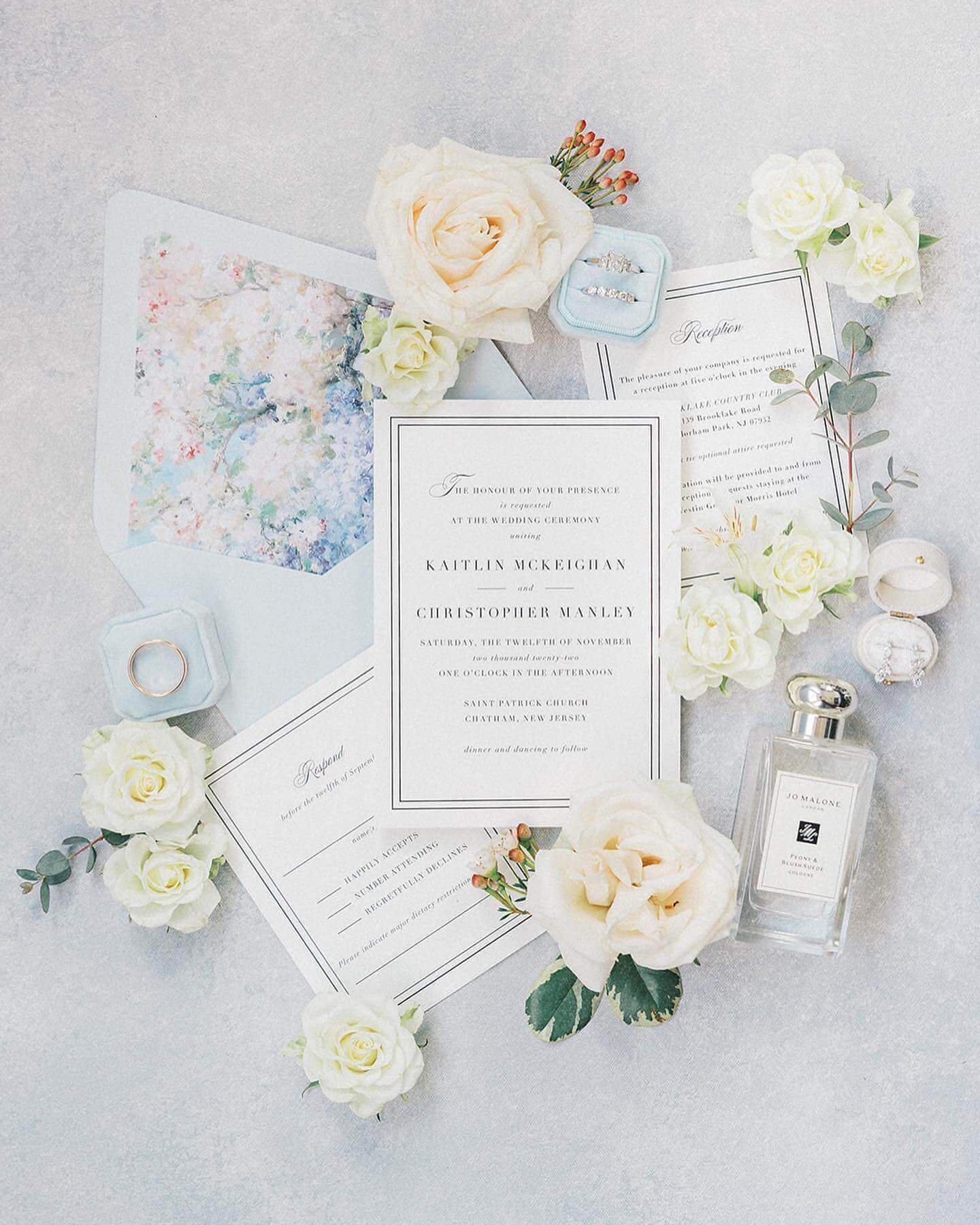 A blue and white wedding invitation adorned with flowers and accompanied by a bottle of perfume, perfect for couples seeking gorgeous florham park wedding venues in New Jersey.
