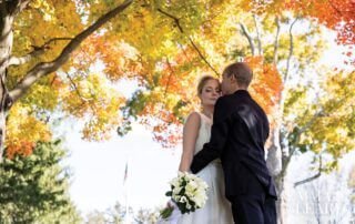 A couple, bride and groom, embracing under a tree in the fall at a beautiful wedding venue in Florham Park, NJ.