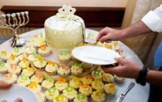 At a kosher wedding in NJ, a man is cutting a cake in front of a table full of cupcakes.