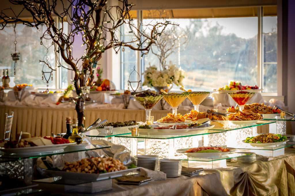 brooklake-cuisine-food An elegant buffet table setup boasts various dishes, including salads, fruits, and appetizers, gracefully arranged on glass shelves. In the foreground, a decorative tree centerpiece adds charm, perfect for celebrating special moments like getting your marriage license in NJ.