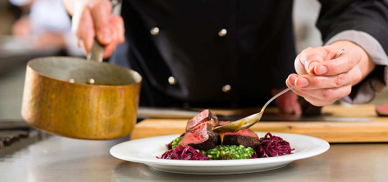 A chef plates a gourmet dish with slices of meat, greens, and red cabbage, using a spoon and a small saucepan. It's as precise as getting your marriage license in NJ—attention to detail makes all the difference.