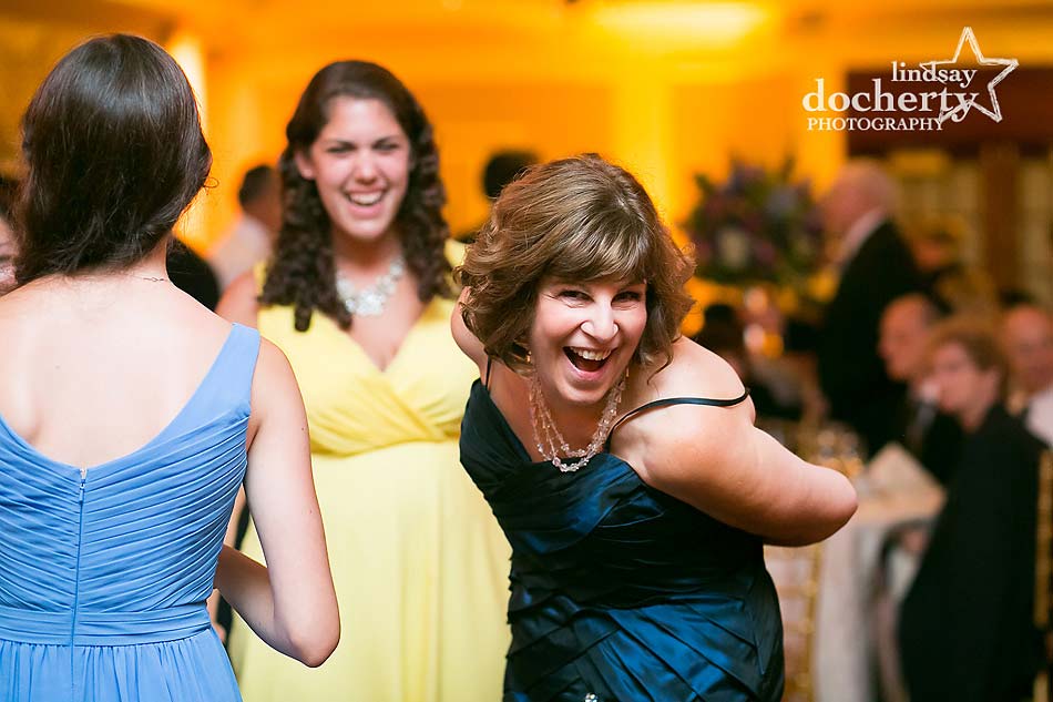 Guests at Love Stories at Brooklake, in formal attire, are smiling and dancing joyously at the indoor event.