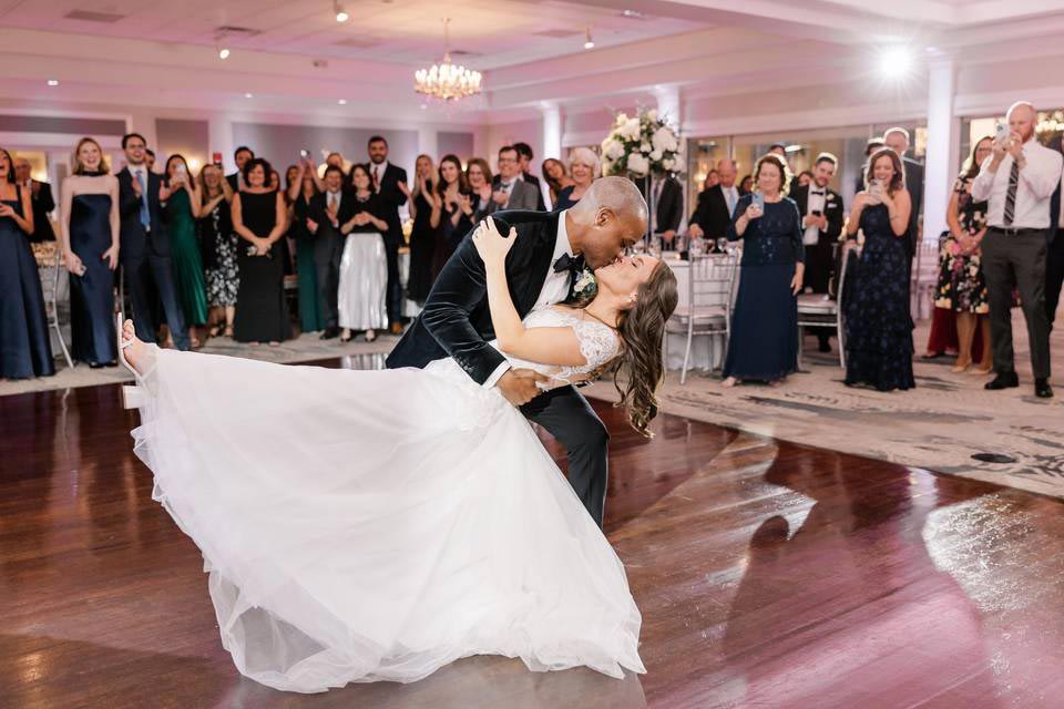 bride-and-groom-dancing-at-brooklake A couple performs a graceful dip dance move on the polished wooden floor of an NJ wedding venue, surrounded by applauding guests.