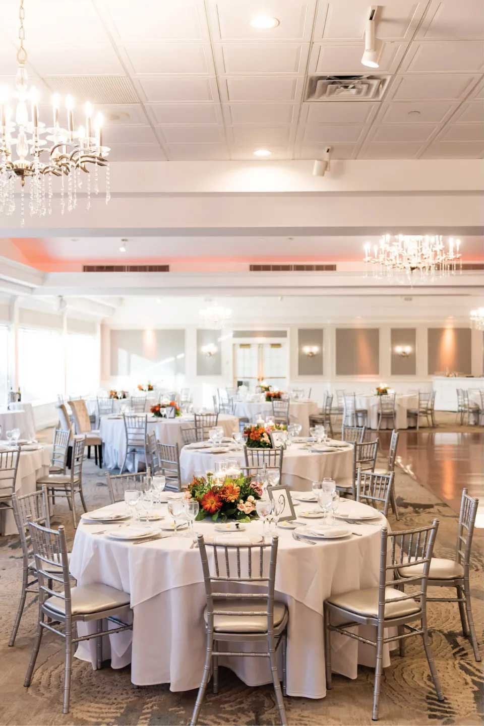 simple-autumnal-wedding-reception A stunning nj wedding venue, this banquet hall features round tables with white tablecloths, silver chairs, elegant floral centerpieces, and sparkling chandeliers.