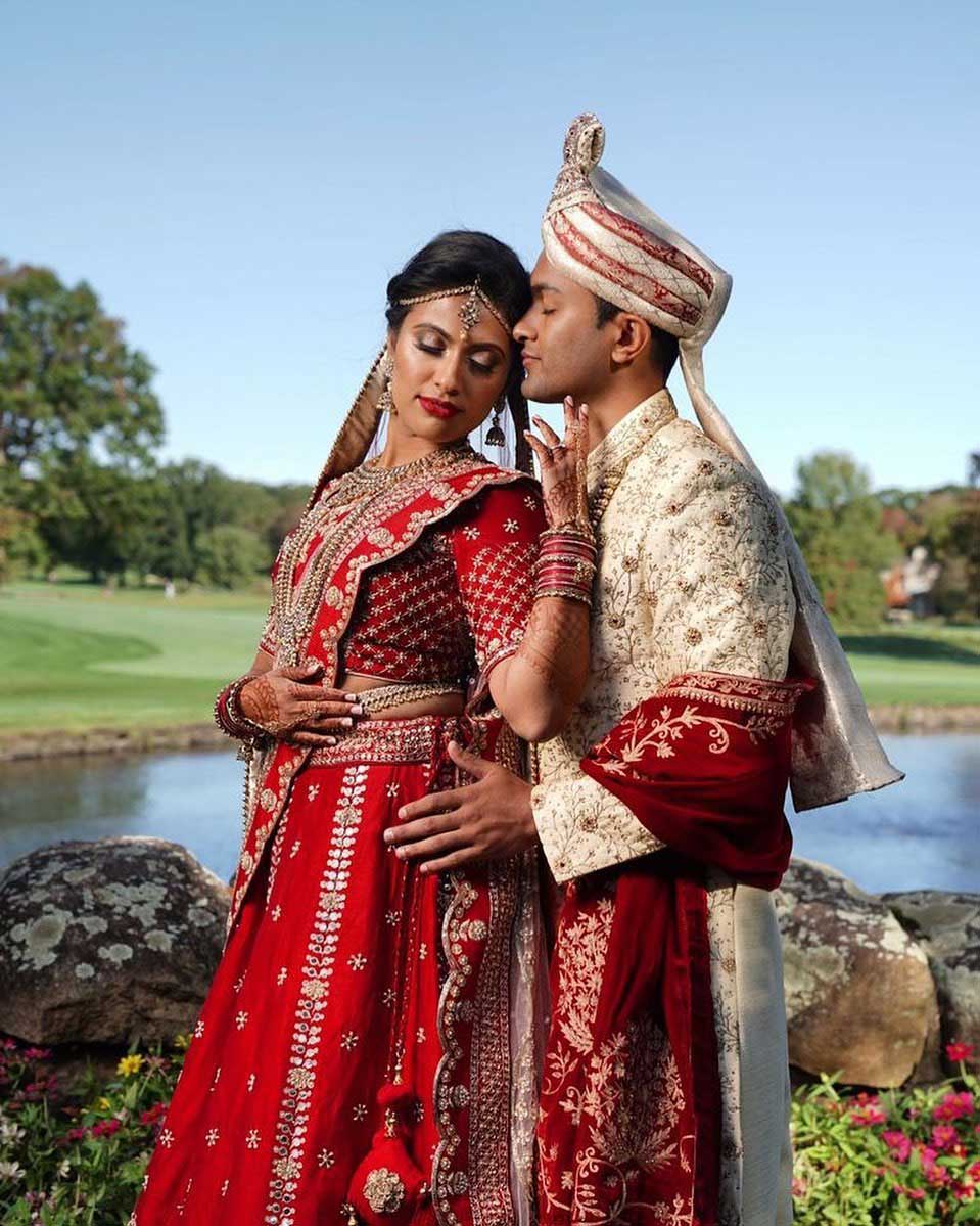 brooklake-indian-south-asian-bride-groom-by-lake A couple in traditional Indian wedding attire poses outdoors by a pond; the woman wears a red lehenga, and the man wears an embroidered sherwani and turban, celebrating love in style—perfect inspiration for NJ Teen Events.