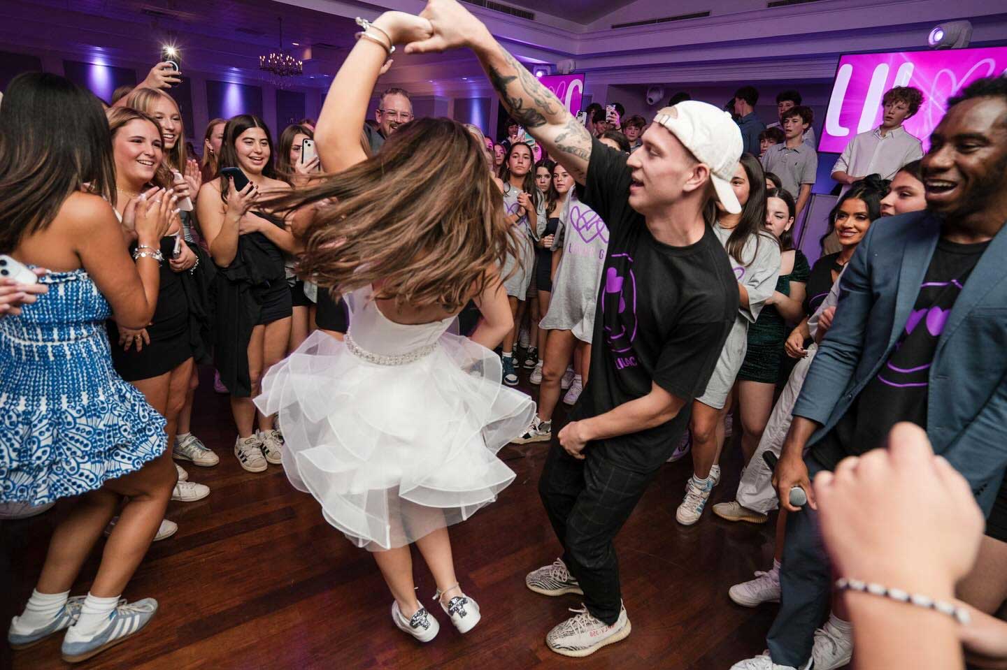 exciting-bat-mitzvah-dancing-at-brooklake A crowd watches as a young woman in a white dress spins while dancing with a man in a black shirt at an NJ Teen Events indoor celebration.