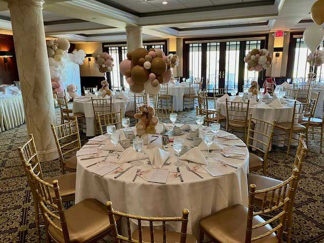 waterford-room-baby-shower-tables A banquet room with round tables set for an event, featuring white linens, gold chairs, balloon centerpieces, and teddy bear decorations—perfect for memorable NJ Teen Events.