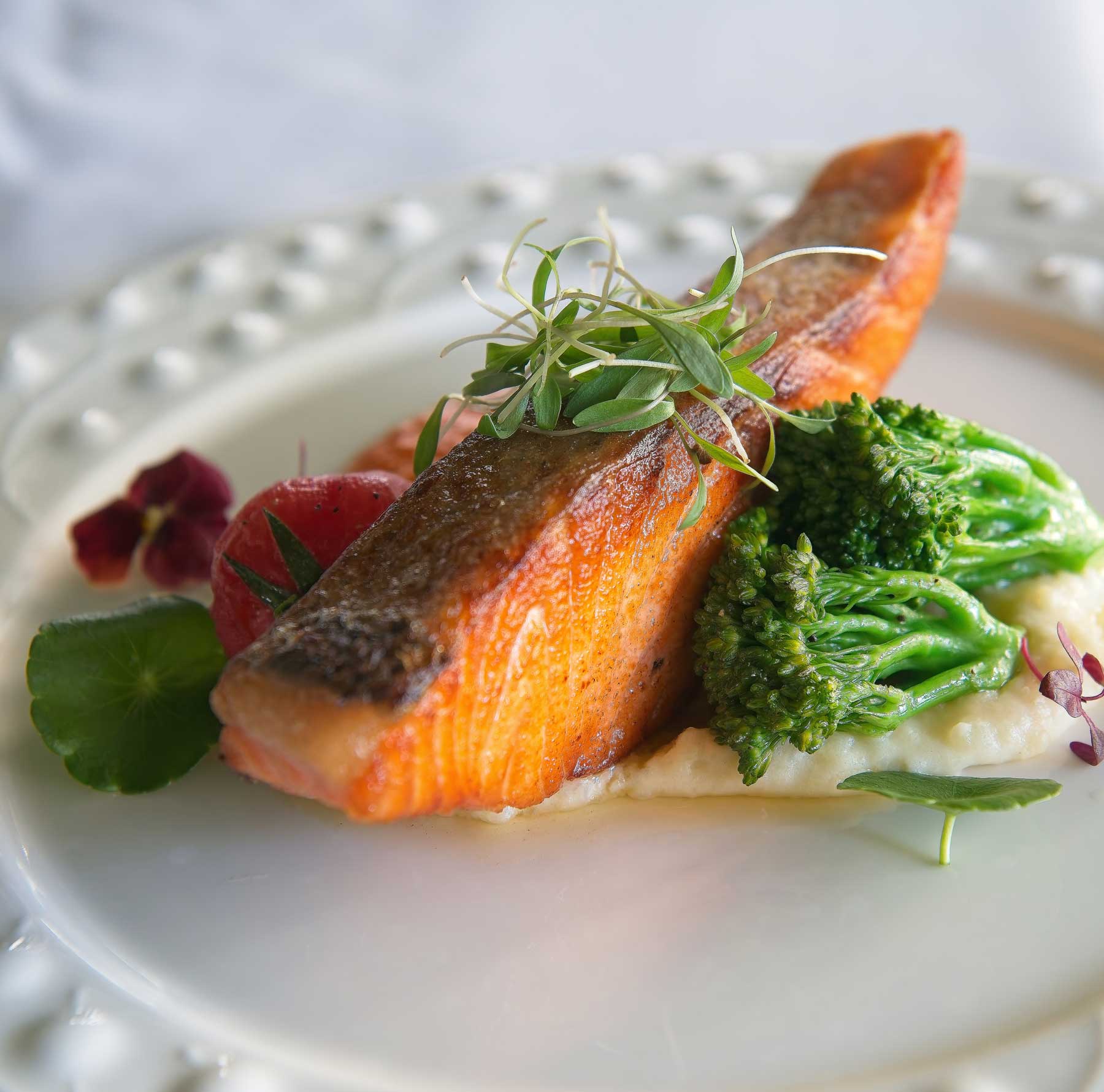 brooklake-entree-dinner-plated A plate with a seared salmon fillet on mashed potatoes, topped with microgreens, served with broccoli, and garnished with edible flowers—perfect for sophisticated Wedding & Event Cuisine.