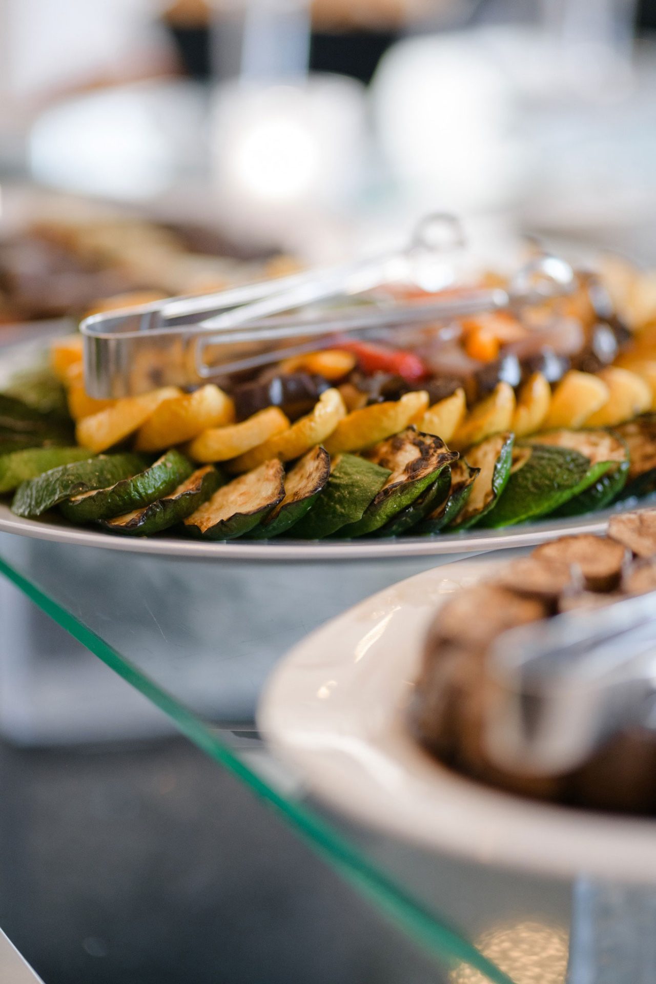 grilled-vegetables-station-cocktail-hour A platter of grilled vegetables, including zucchini and yellow squash, served with metal tongs on a buffet table—perfect for wedding & event cuisine.