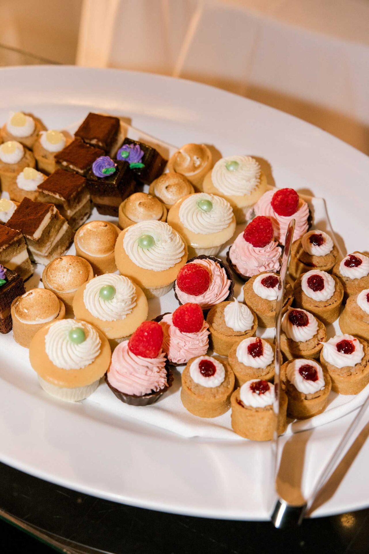 pastries-at-Brooklake A white plate with an assortment of mini desserts, perfect for Wedding & Event Cuisine, featuring cupcakes with pink frosting, cream-topped tarts with berries, and layered chocolate squares.