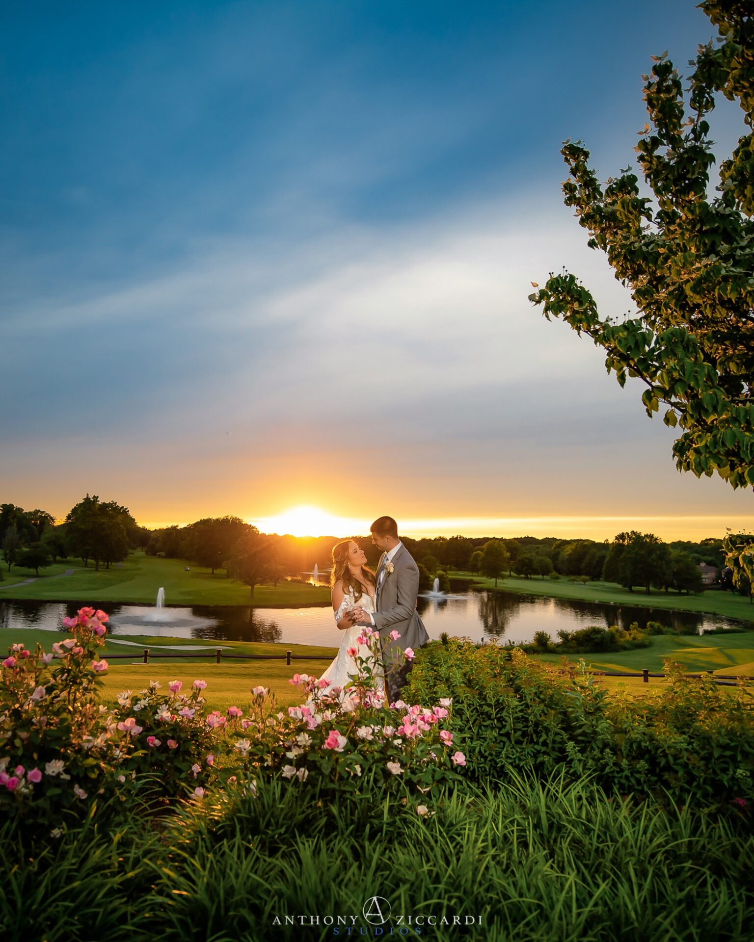 brooklake-property-bride-groom-616836483_1460006486136041_1862332159299461342_n A bride and groom stand together in a garden at an elegant NJ wedding venue, with a pond, fountain, and golf course behind them at sunset.